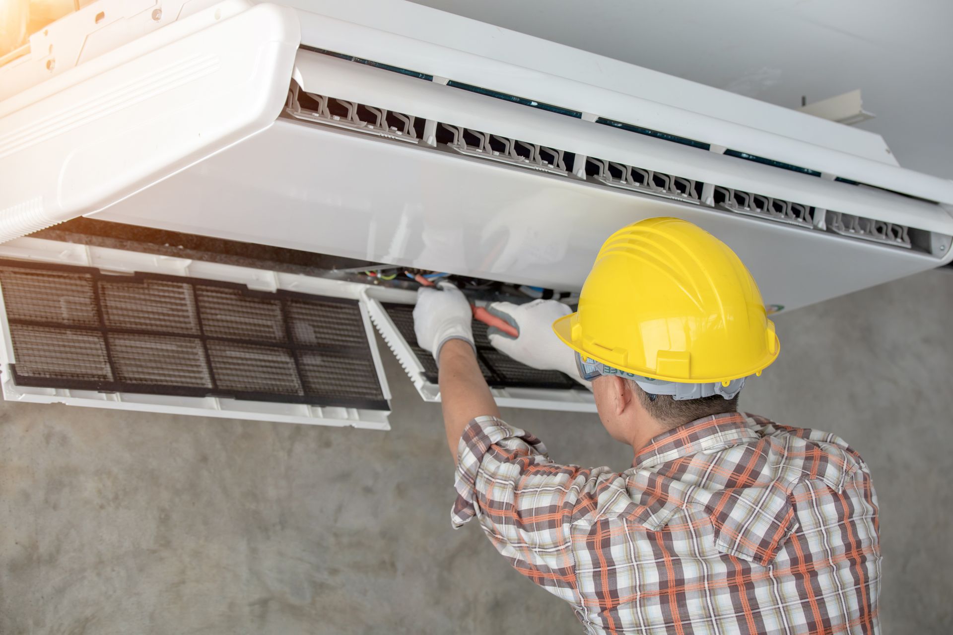 Technician in yellow hard hat repairing a wall-mounted air conditioner indoors Technician in yellow hard hat repairing a wall-mounted air conditioner indoors