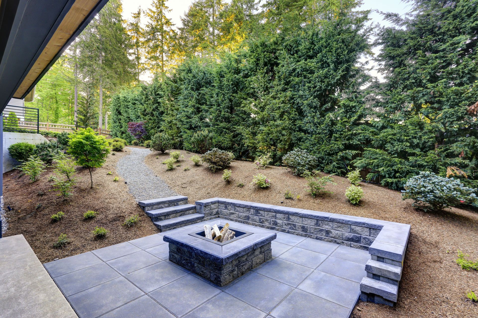 Backyard patio with fire pit, stone retaining walls, and lush greenery.