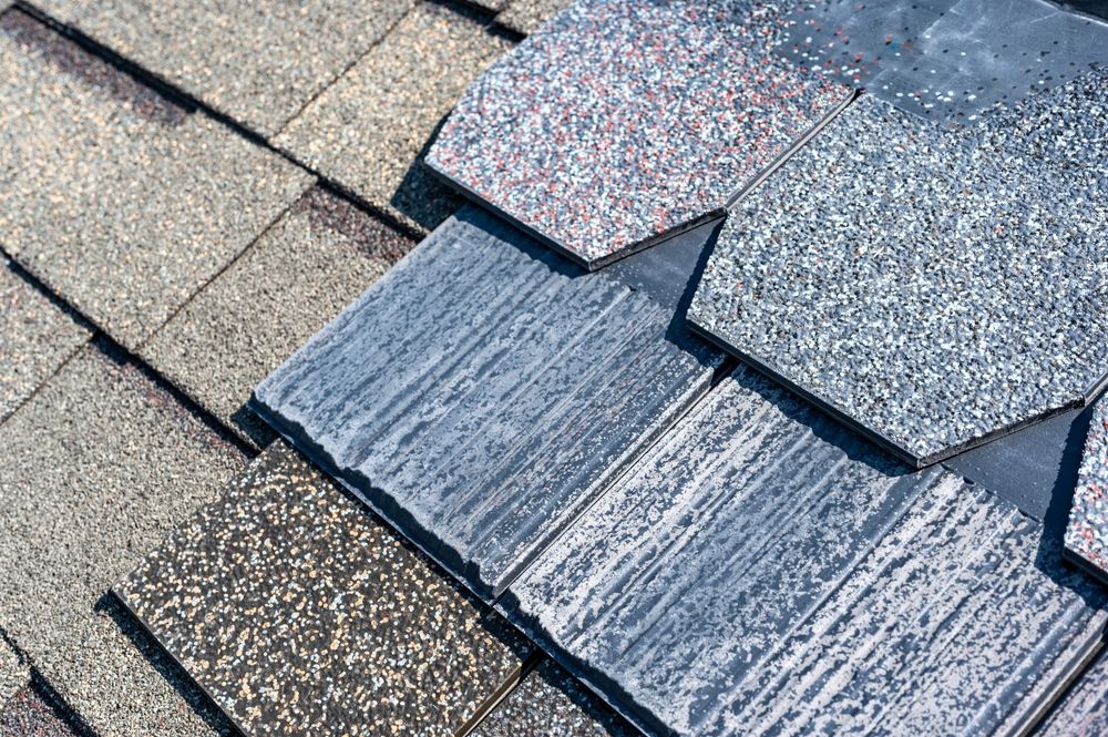 Close-up of overlapping roofing shingles in gray, beige, and speckled blue-gray.