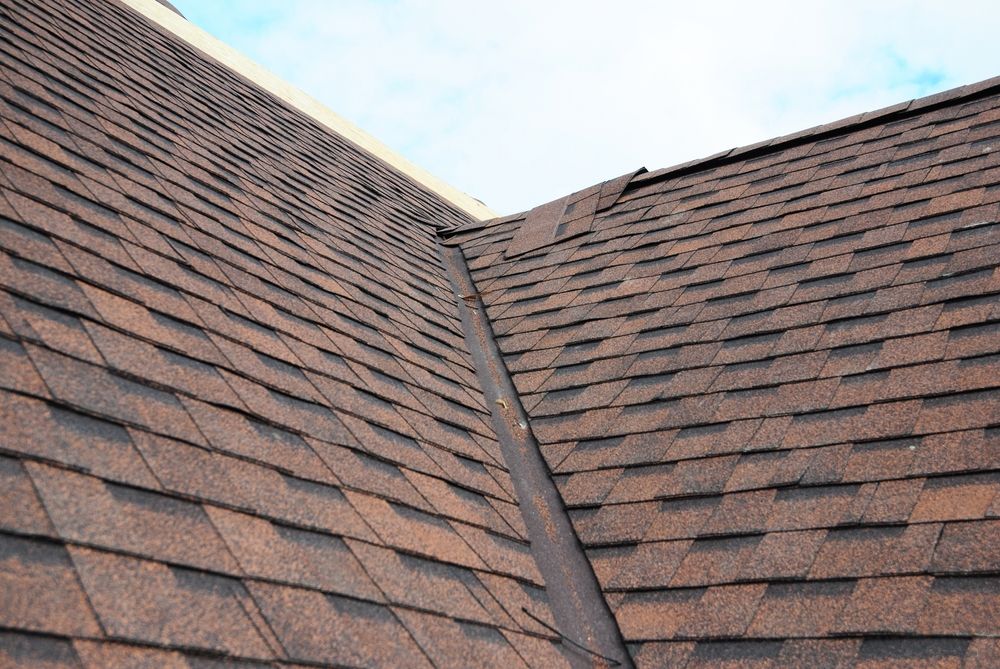 Close-up of a shingled roof with a valley seam against a partly cloudy sky
