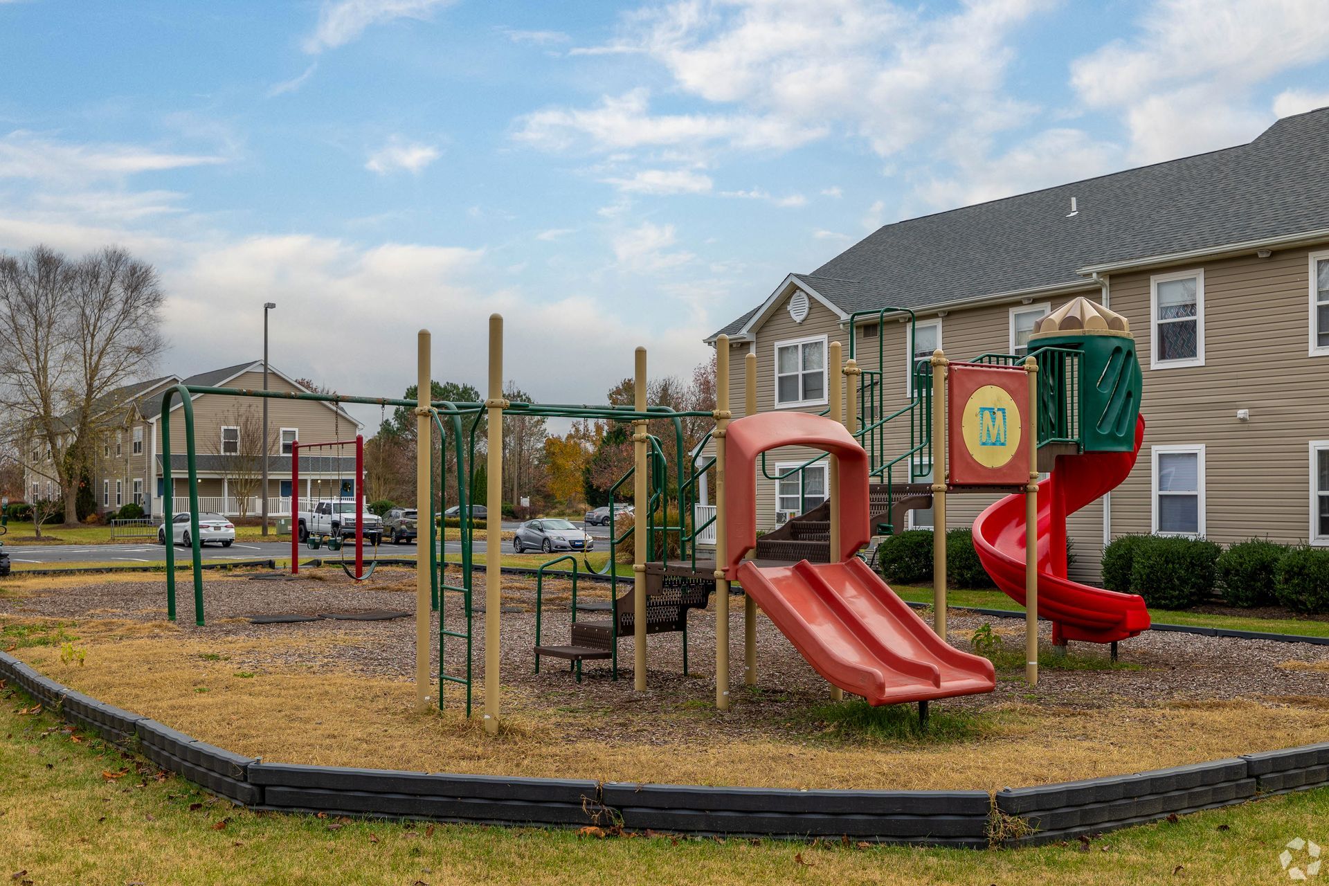 Playground with slides, swings, and climbing bars in front of apartment buildings on a cloudy day.