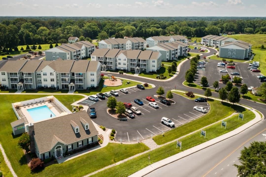 Apartment complex with multiple buildings, a pool, and parking. Green grass surrounds.