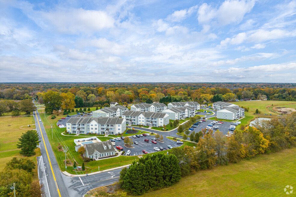 Aerial view of apartment complex surrounded by trees and fields, with road in the foreground.