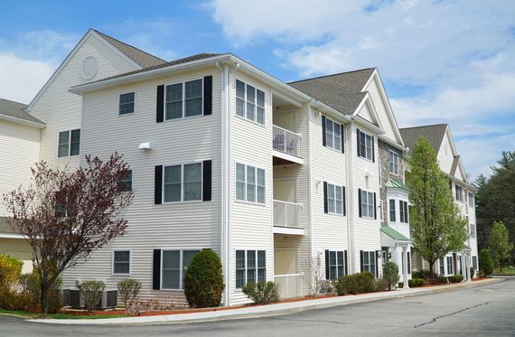 White multi-story apartment building with black shutters and balconies, grey roof, blue sky.