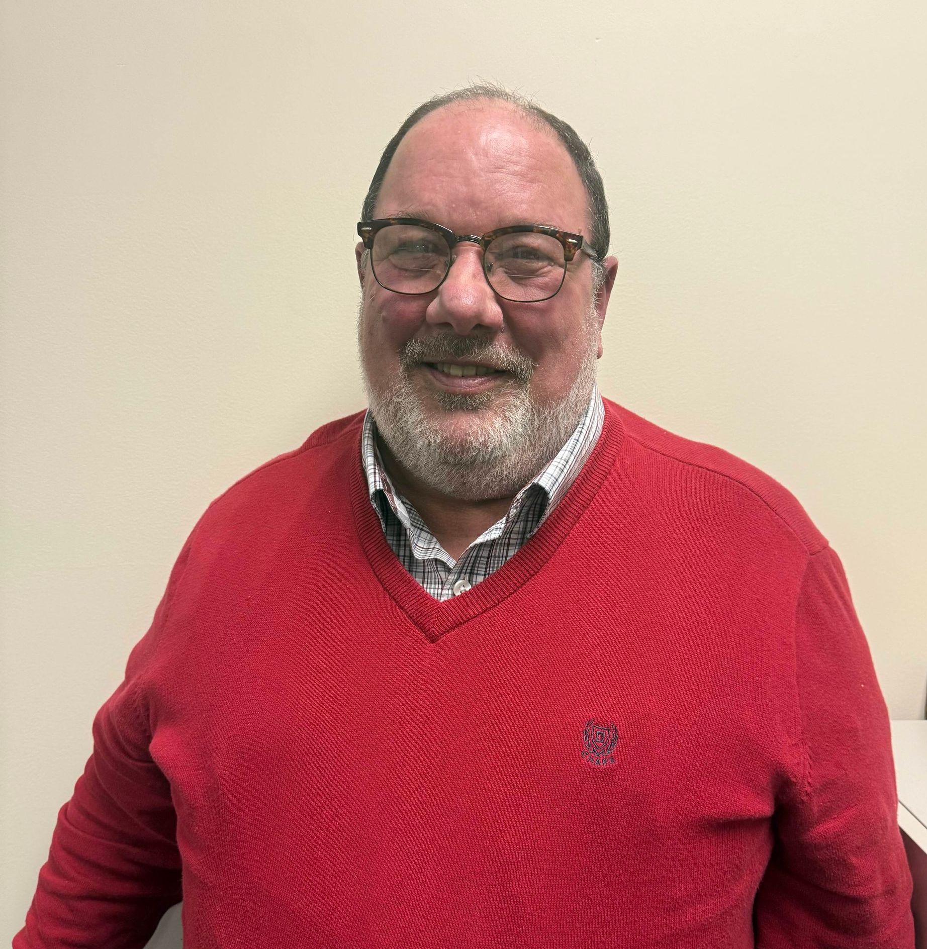 Smiling man in glasses and red sweater standing against a plain beige wall