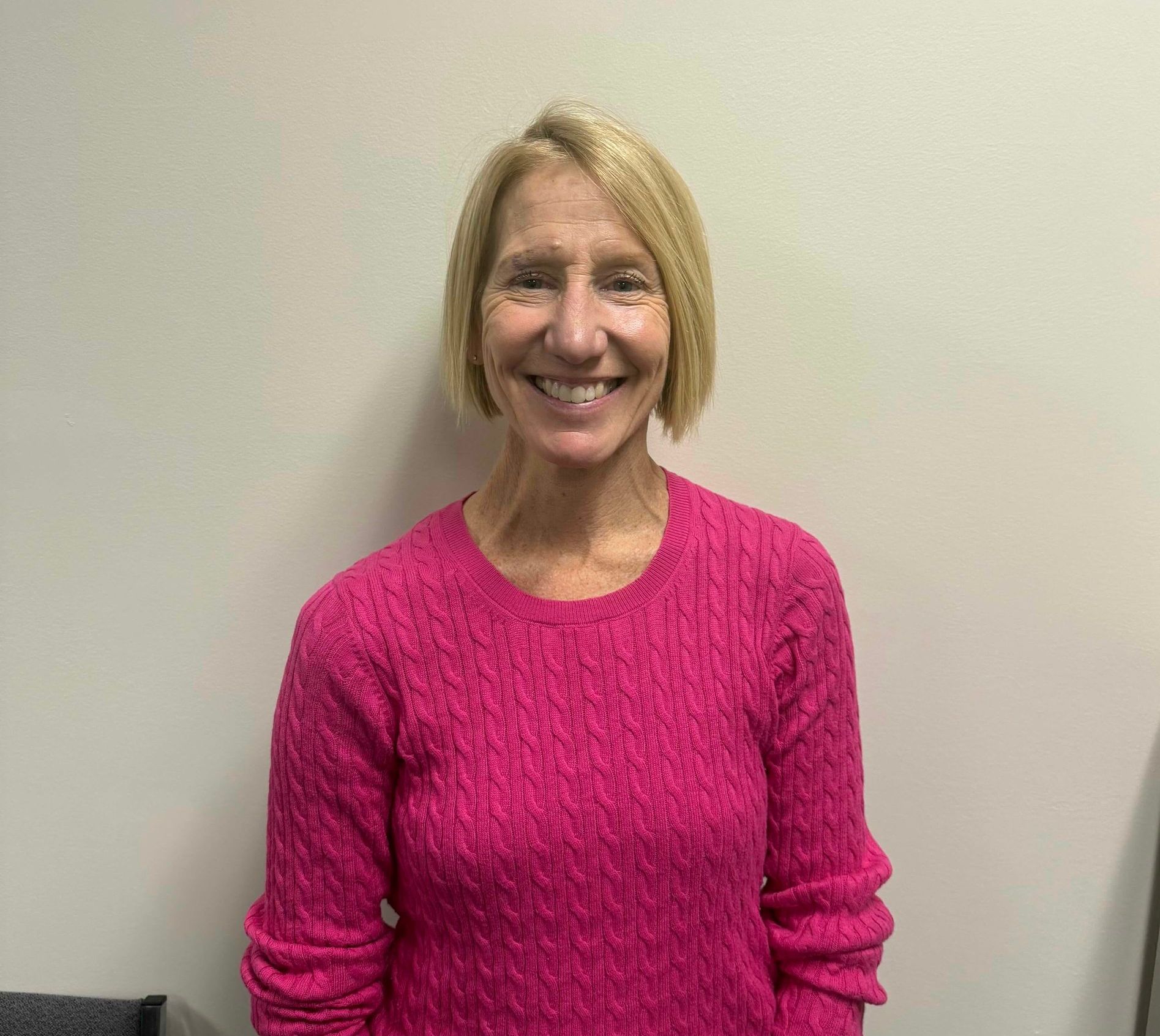 Smiling woman in a bright pink sweater standing against a plain wall