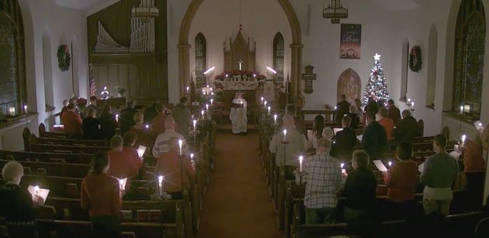 Church congregation seated in candlelit pews during a Christmas service with decorated altar and tree
