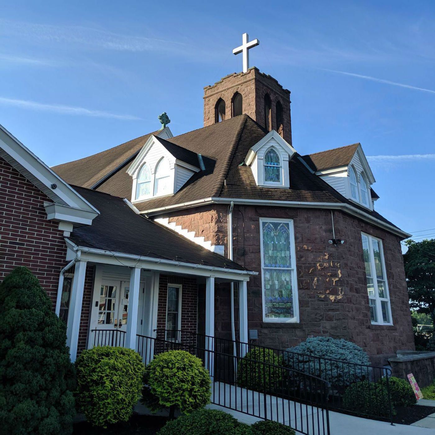 Brick church with white cross on steeple and small front entrance under a blue sky