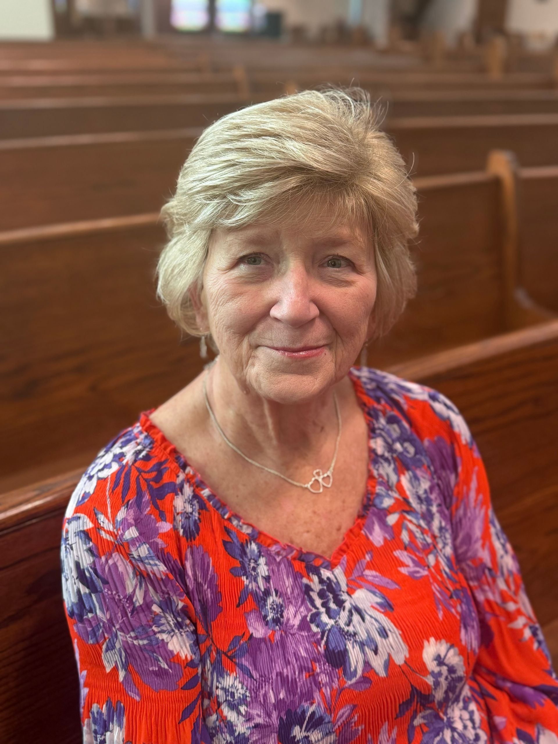 Smiling person in a bright floral blouse seated in a wooden church pew