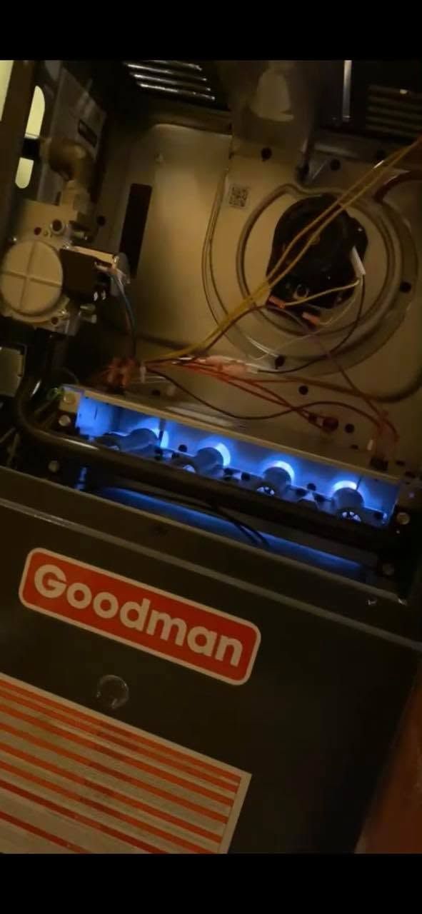 Open furnace with blue burner flames and visible wiring, Goodman unit in basement mechanical room
