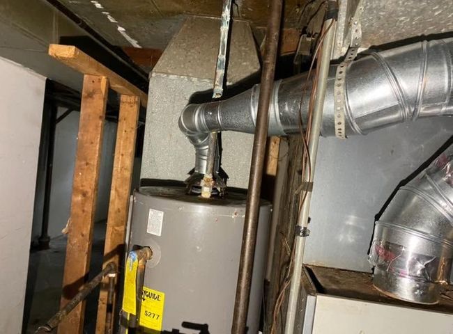 Basement utility area with a water heater and exposed metal ductwork against unfinished walls