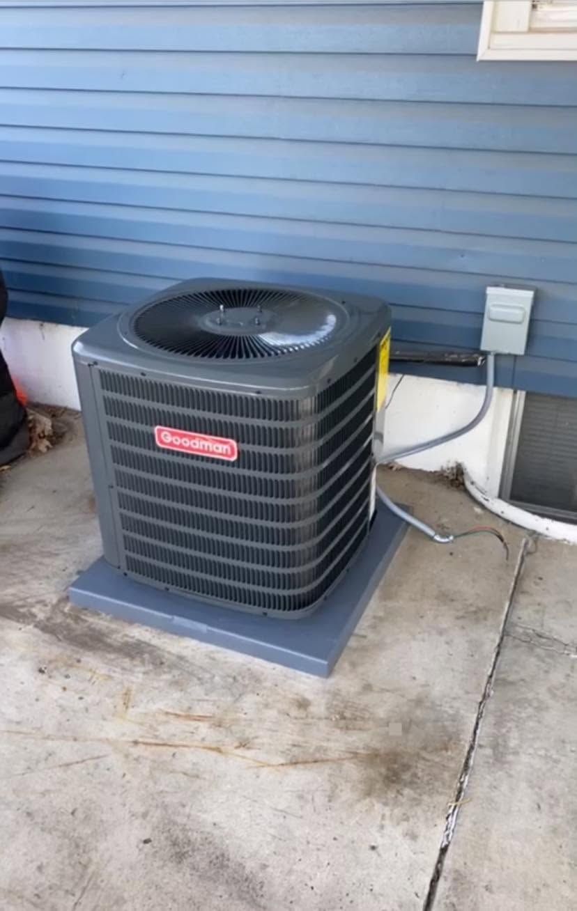 Outdoor air conditioner unit beside a blue house wall on a concrete pad.