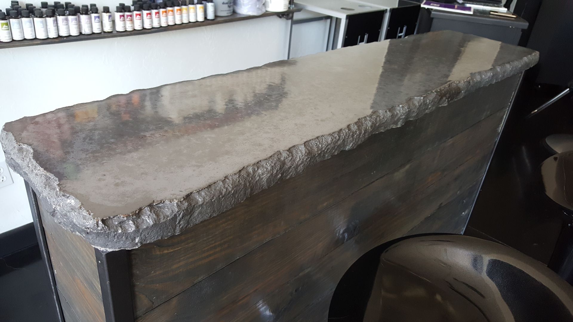 Stone-topped bar counter in a dim interior, with stools and shelves of bottles behind it