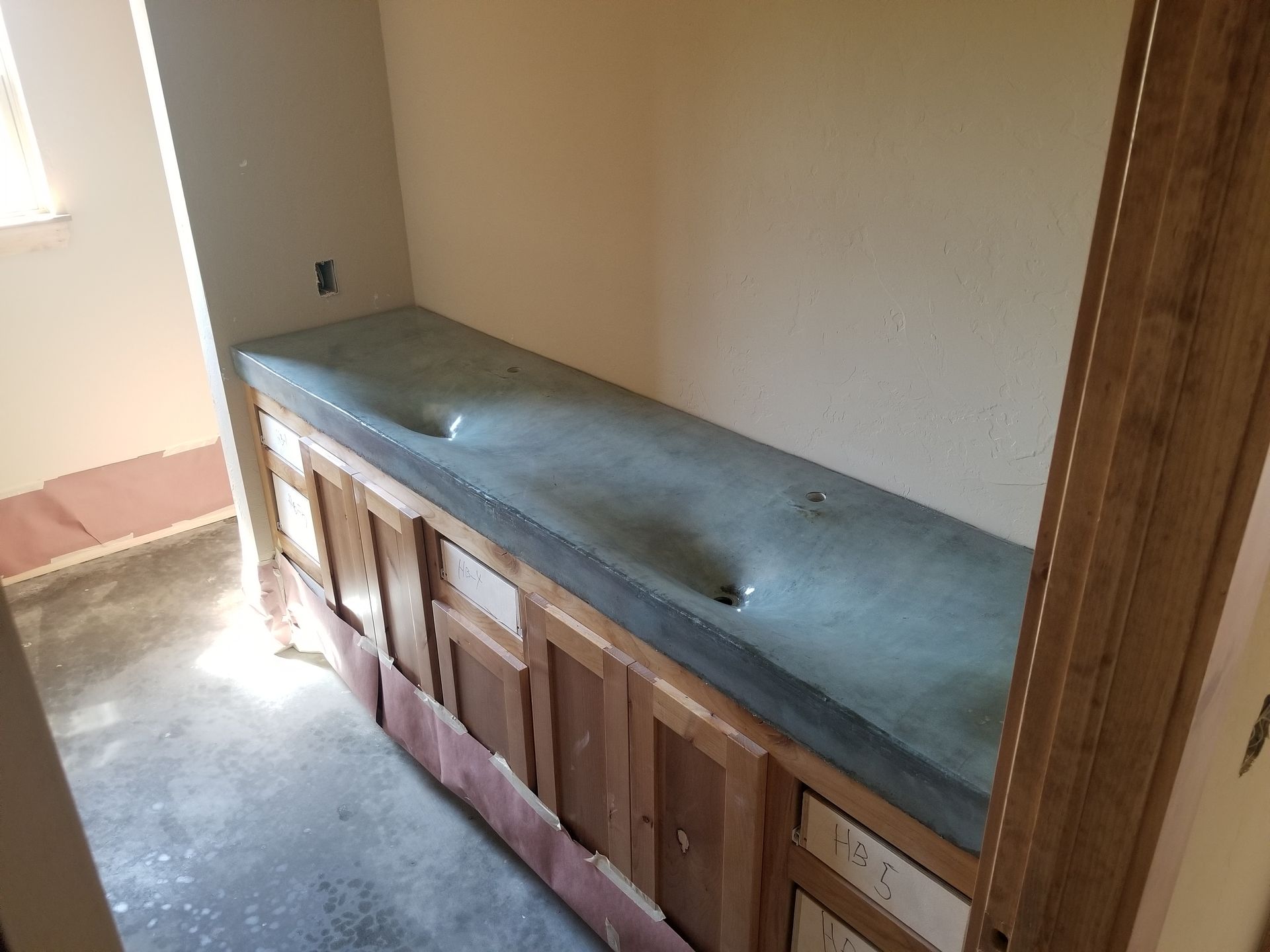 Narrow room with a long wooden cabinet topped by a concrete countertop under construction.