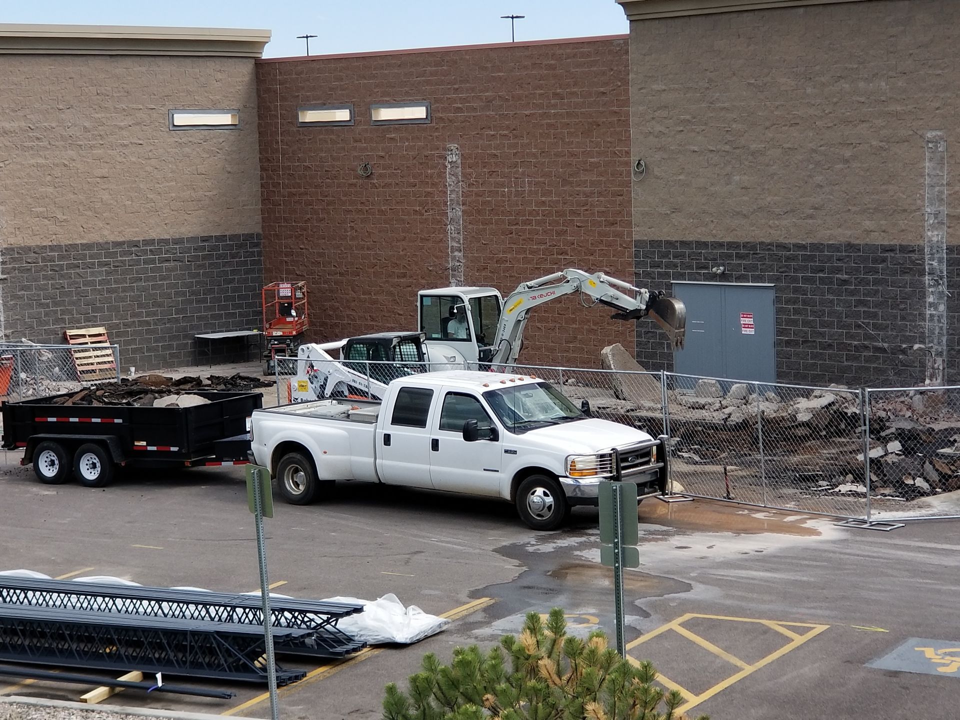 White pickup and excavator at a brick building construction site with debris and a trailer