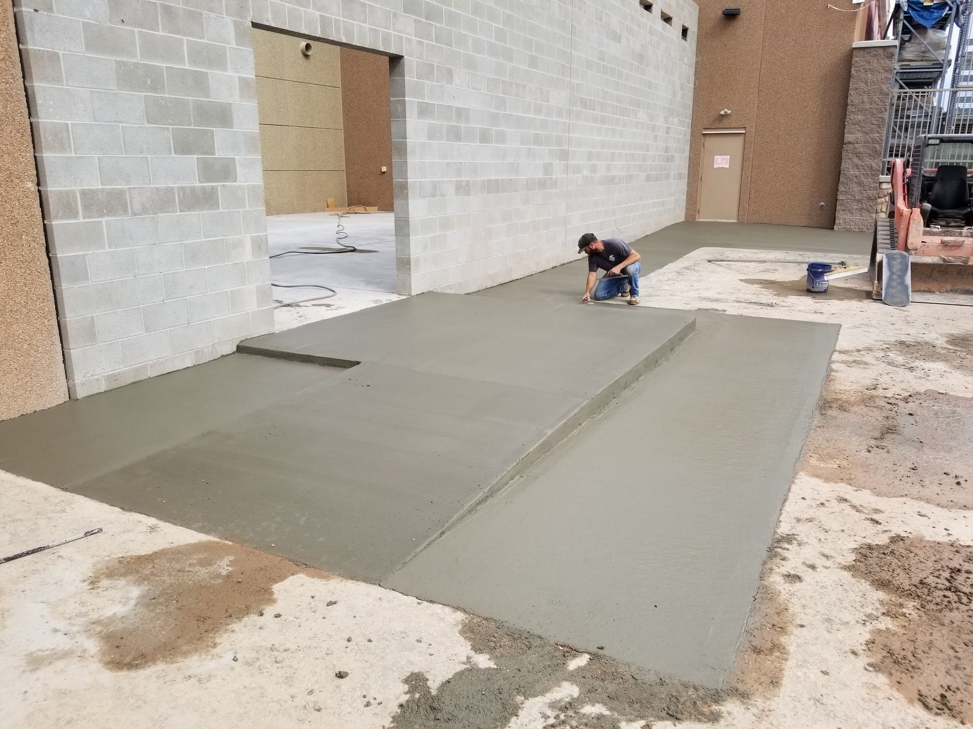 Construction workers smoothing a large concrete slab beside a building under construction.