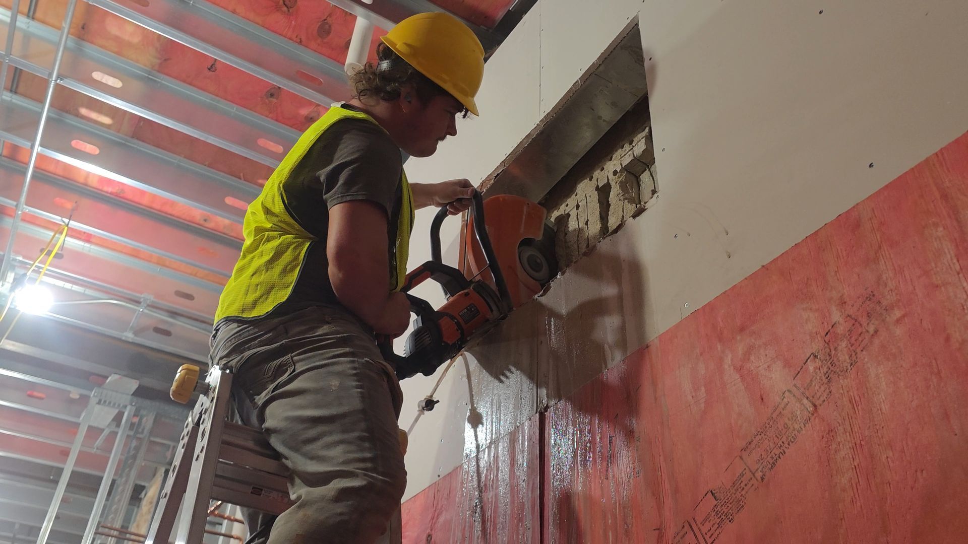 Worker in hard hat using a power saw to cut into a wall on a construction site.