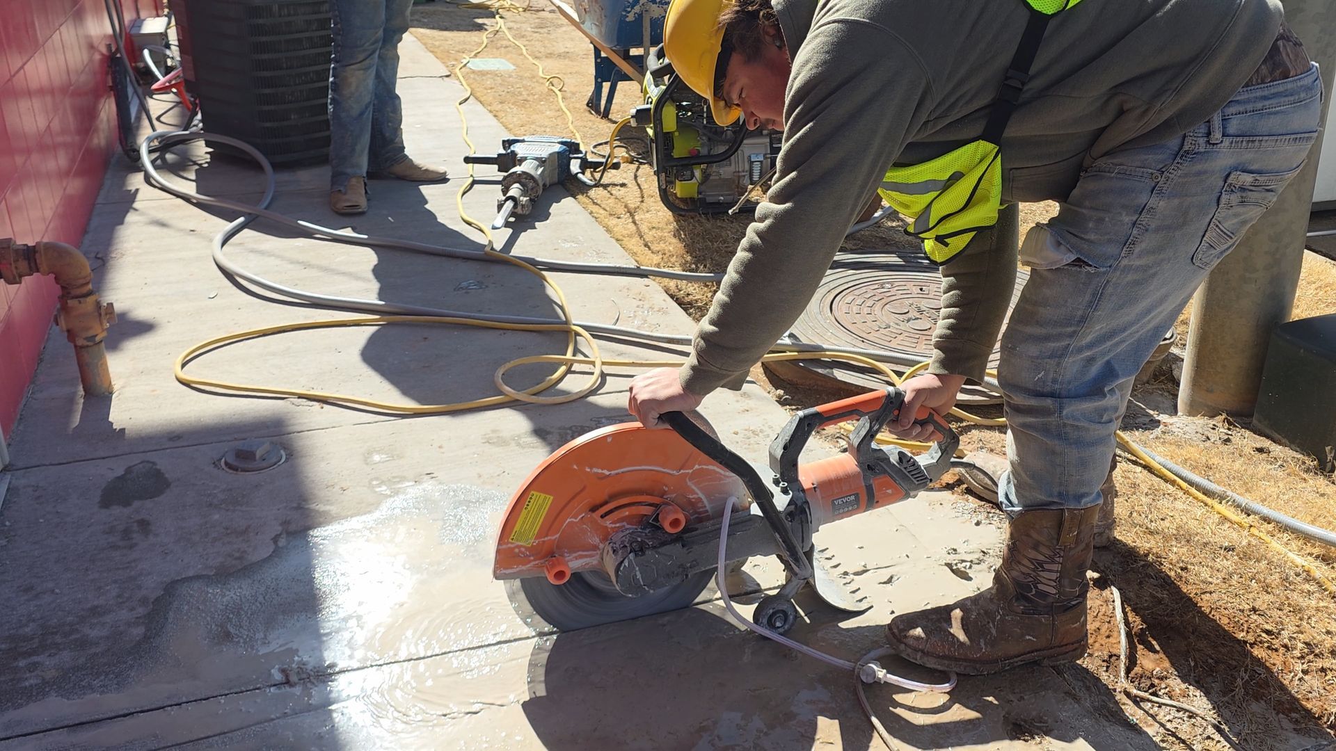Worker using a red concrete saw to cut a slab on a sunny construction site