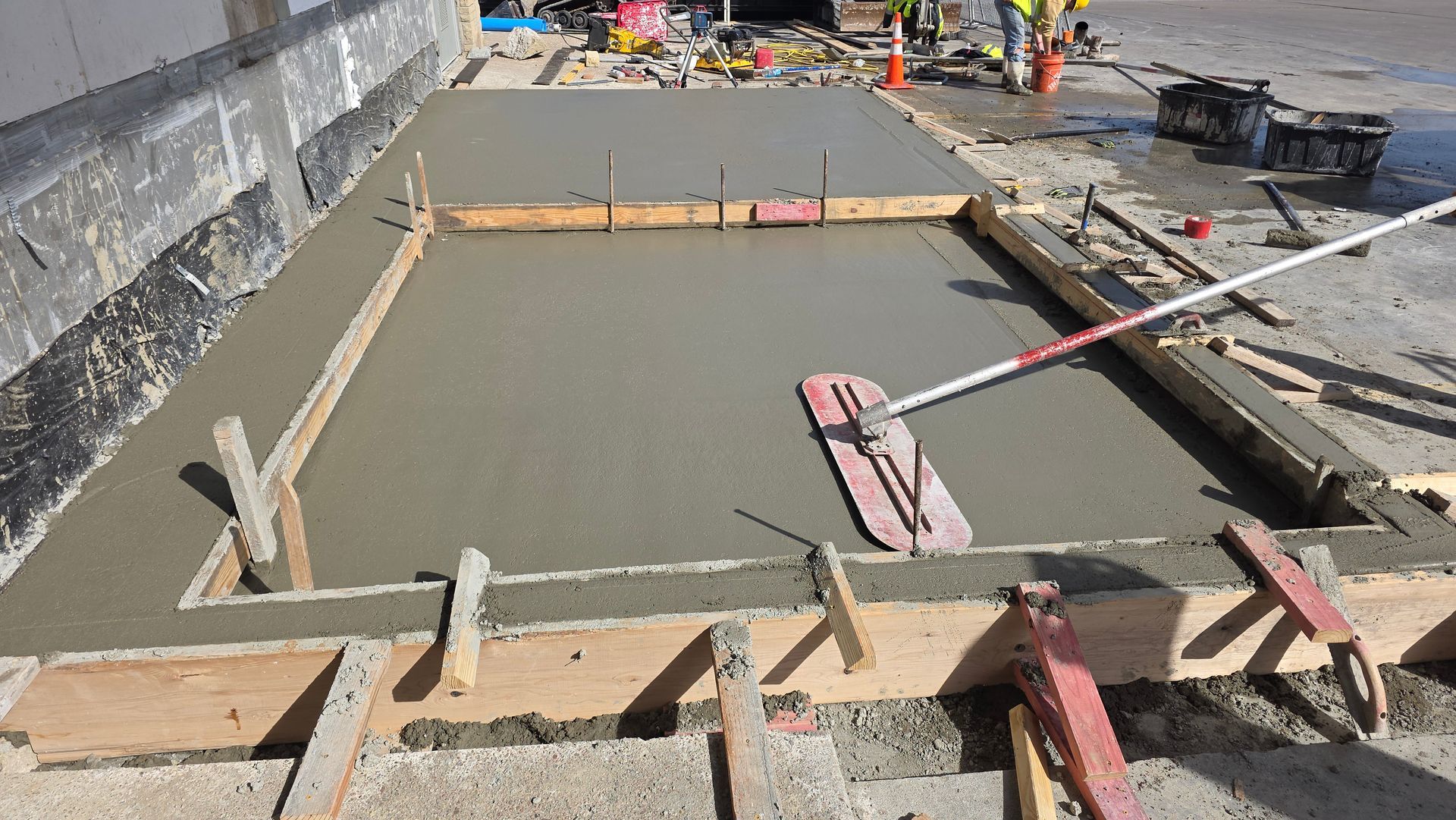 Fresh concrete being screeded in a rectangular construction formwork area near a road.