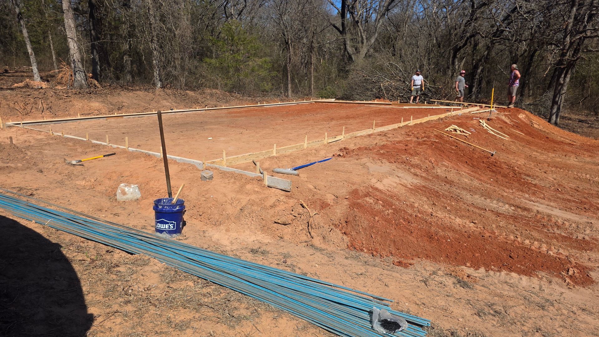 Freshly graded dirt lot with rebar stakes and blue conduit on a construction site