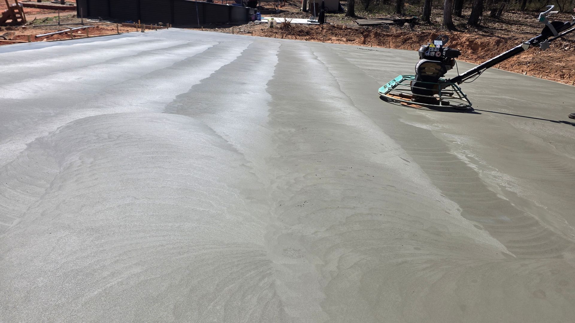 Fresh concrete being smoothed on a residential driveway by a worker with a power trowel