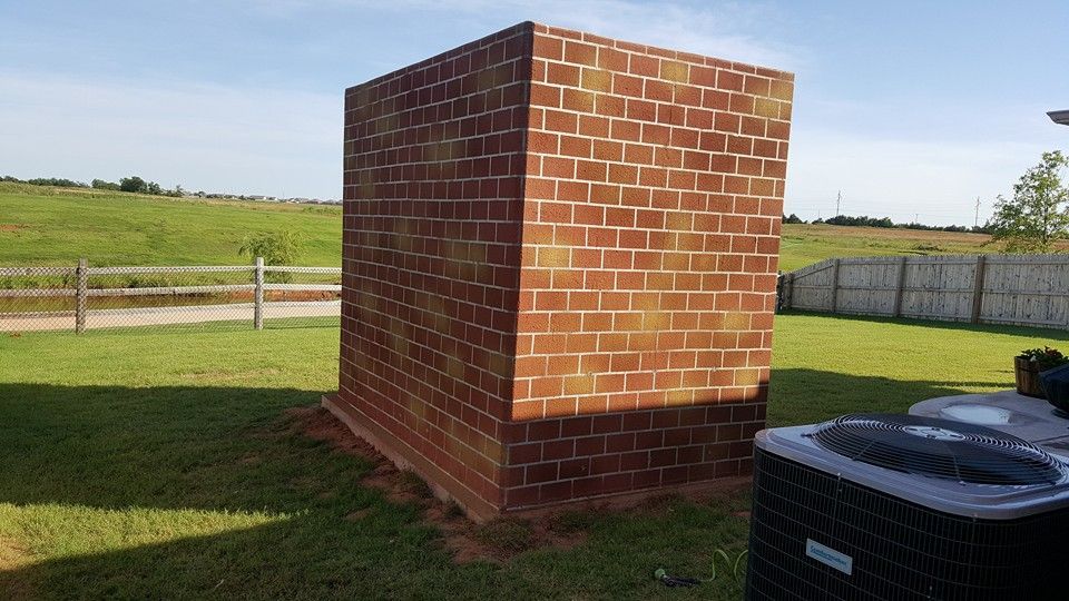 Brick utility structure in a grassy field beside a fence and HVAC unit