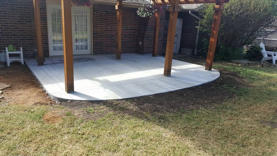 Backyard covered patio with white concrete floor and wooden posts beside a brick house