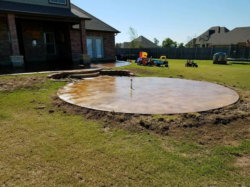Backyard concrete patio under construction beside a brick house on a sunny day
