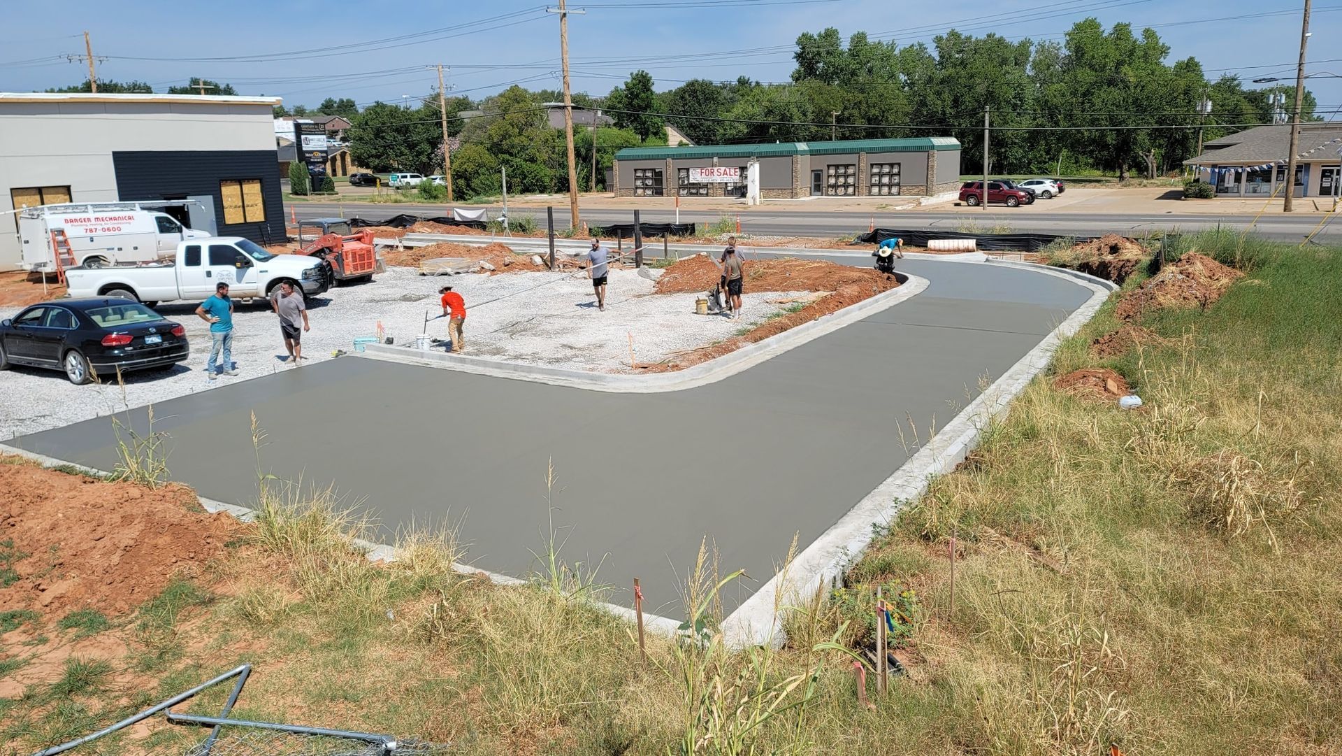 Construction site with fresh concrete foundation, workers, and parked trucks beside a curved driveway