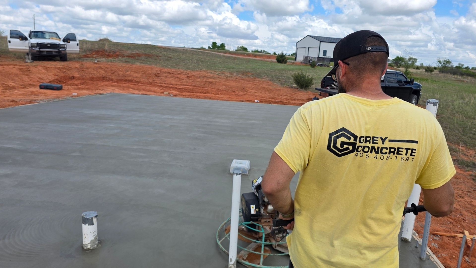 Worker in yellow shirt smoothing fresh concrete slab at a construction site