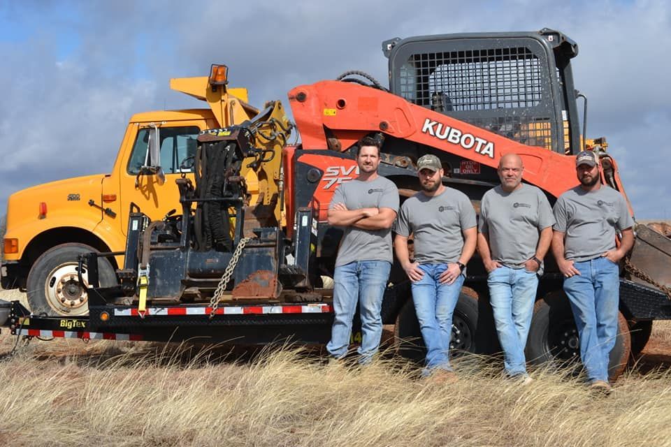 Three men posing on a yellow Kubota utility vehicle in a grassy field under a blue sky