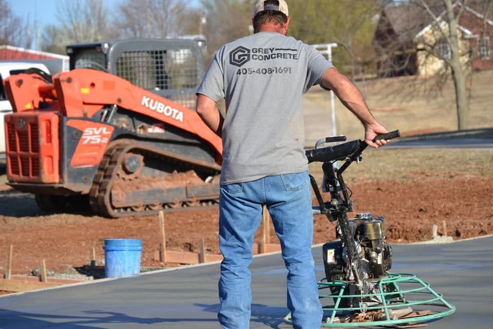 Worker stands behind a concrete finishing machine at a construction site with a Kubota vehicle nearby.