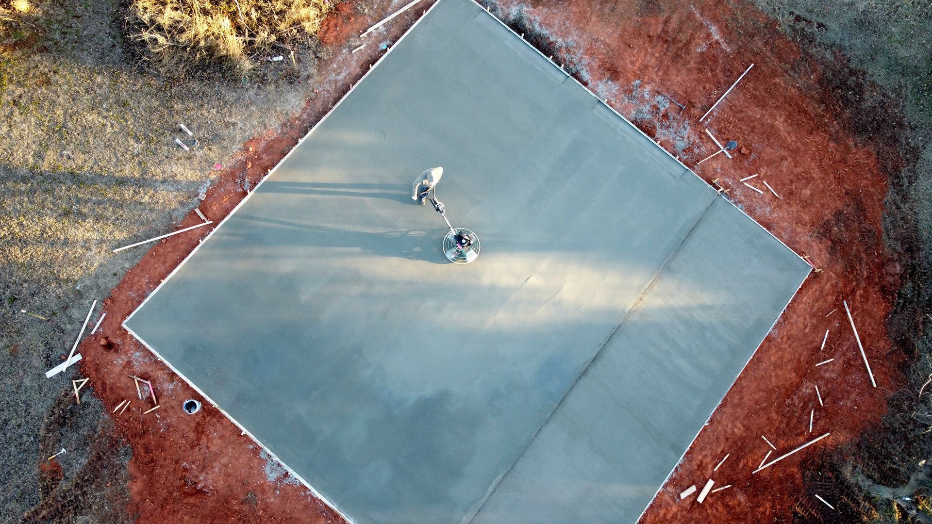 Aerial view of two people standing on a gray square platform surrounded by reddish ground and trees