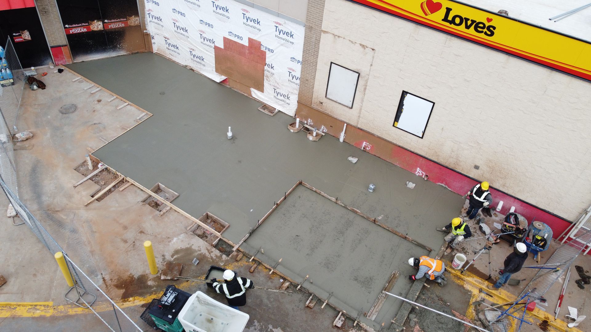 Construction crew pouring concrete at a Lowe’s storefront entrance, with equipment and barricades nearby