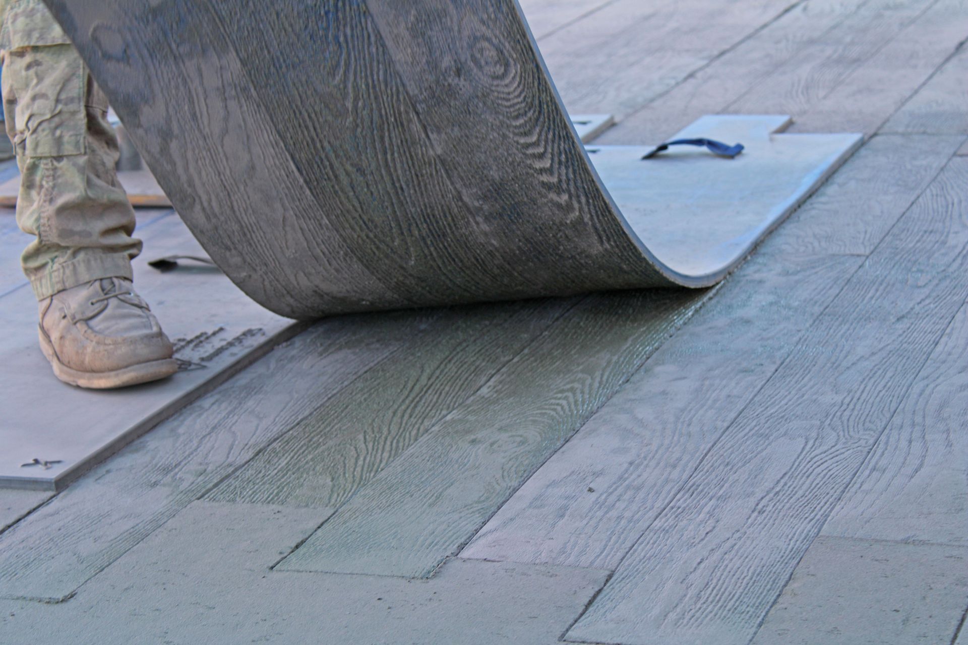 Worker unrolling gray roofing material across a flat rooftop surface
