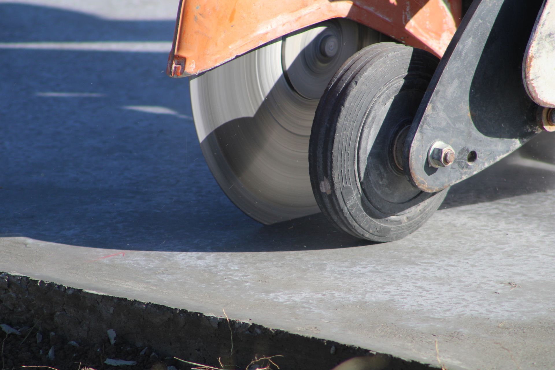 Orange road roller compacting concrete at a street edge