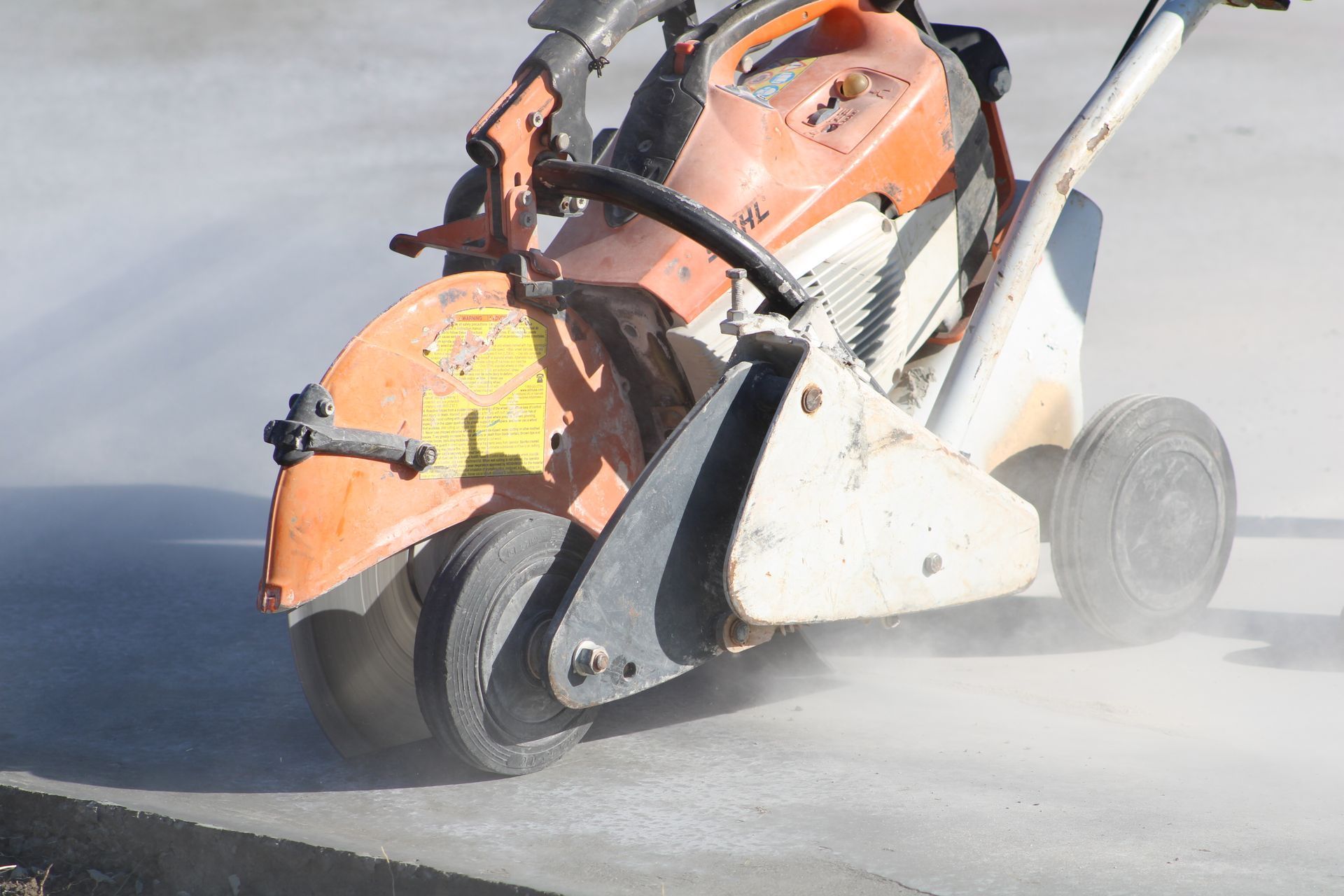 Orange concrete saw cutting pavement, throwing dust as its blade grinds through the road