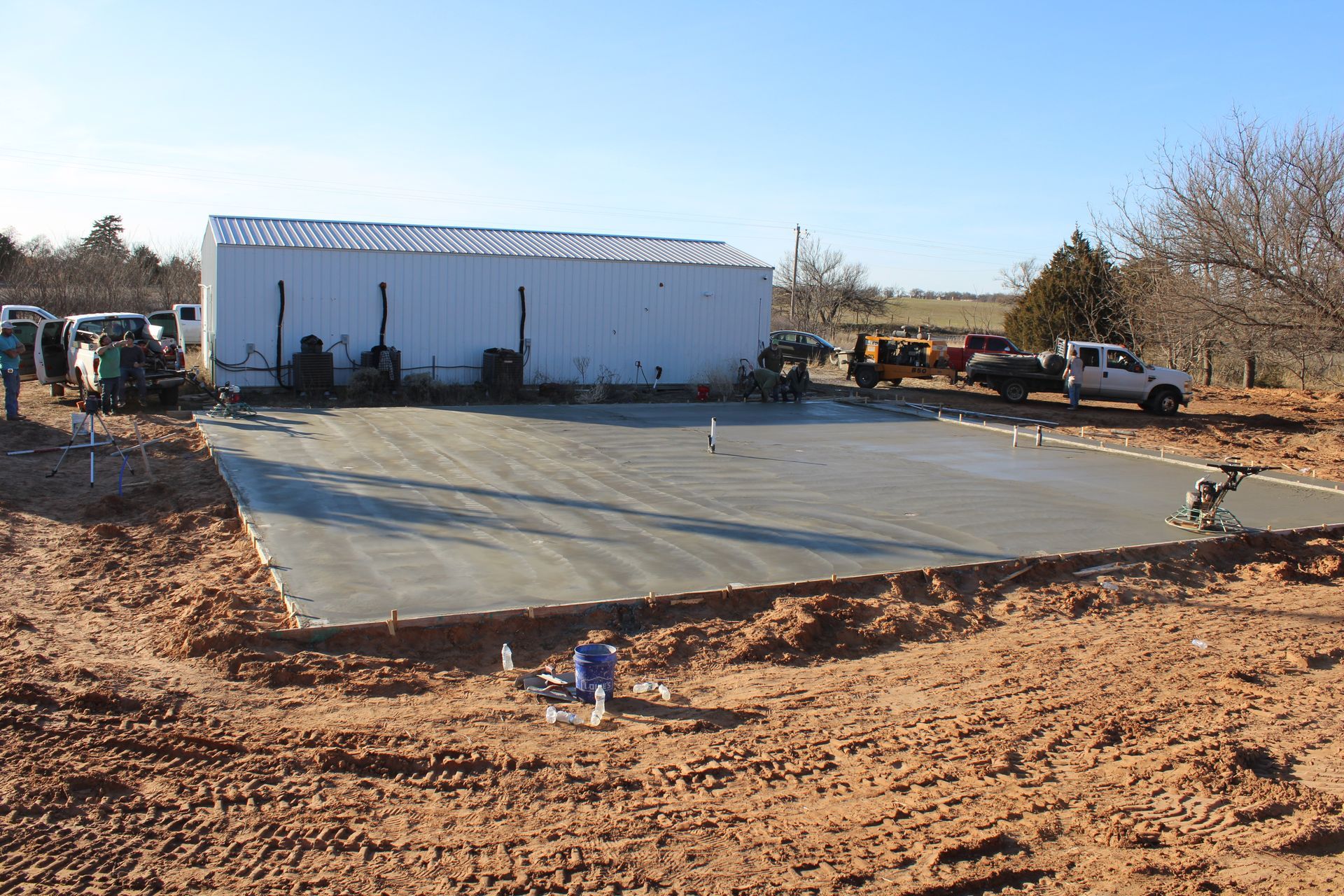 Concrete slab under construction beside a white metal building in a dry, rural lot