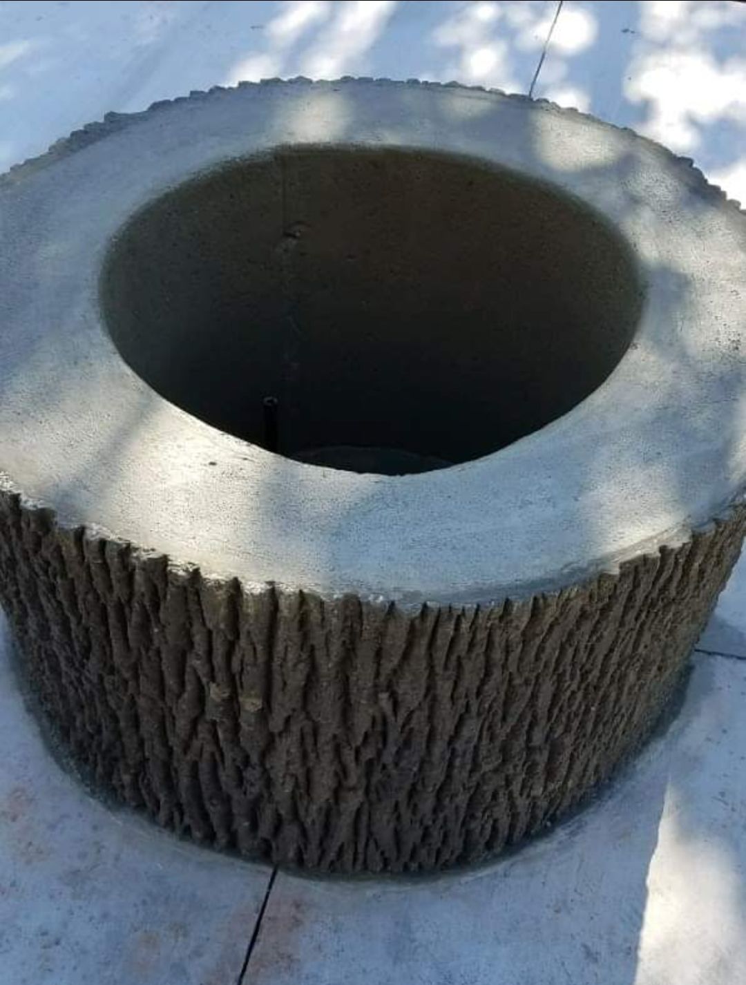 Large hollowed-out tree stump with a smooth cut top, sitting on a paved surface outdoors.
