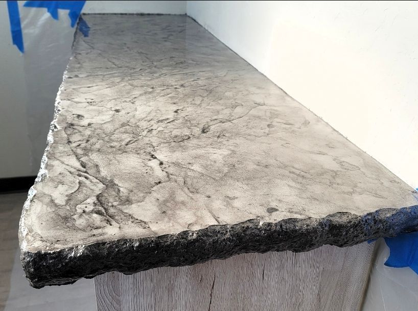 Gray marbled stone countertop with a rough, unfinished edge against a white wall