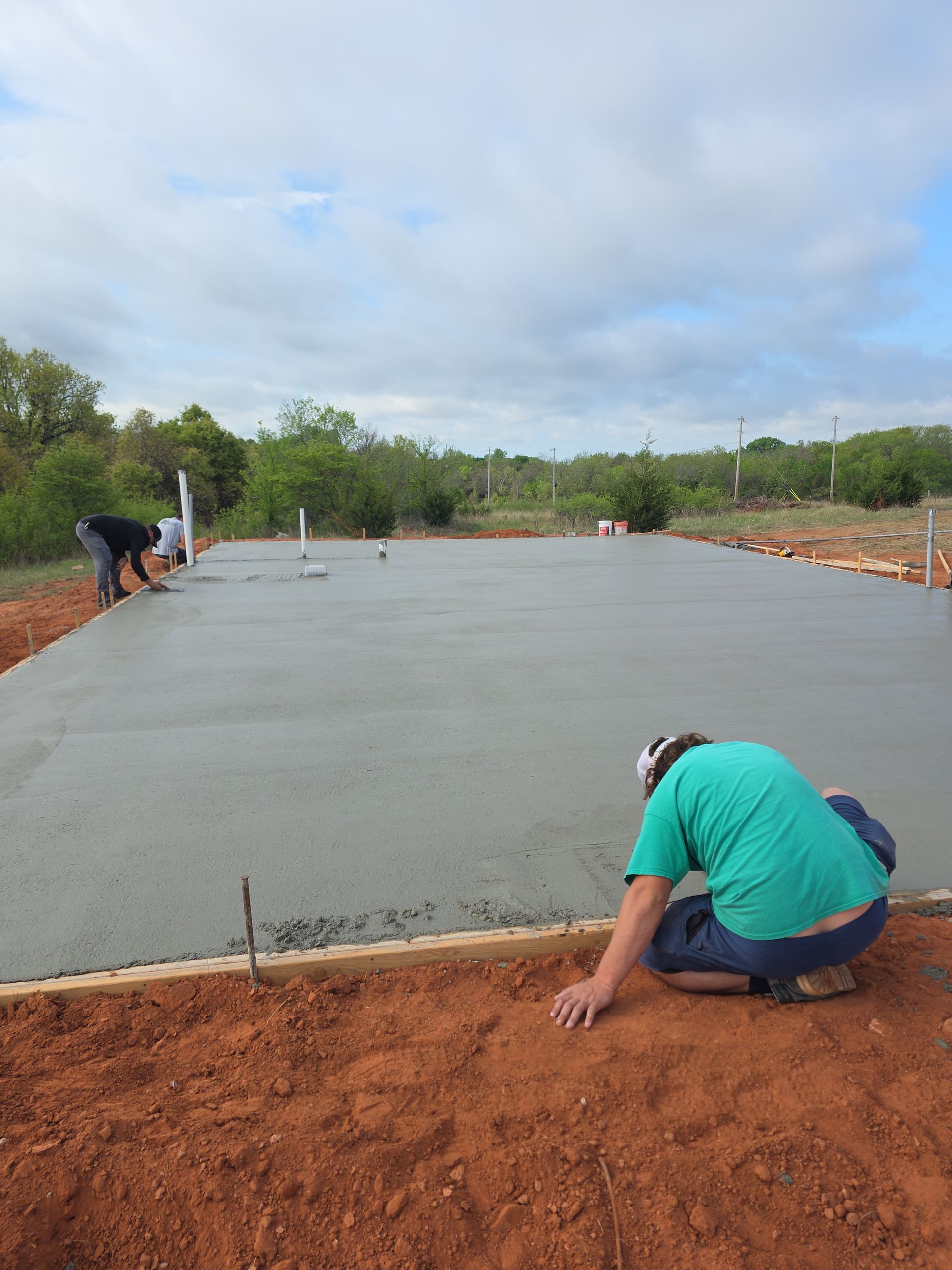 Workers smoothing a large concrete slab at an outdoor construction site under a cloudy sky