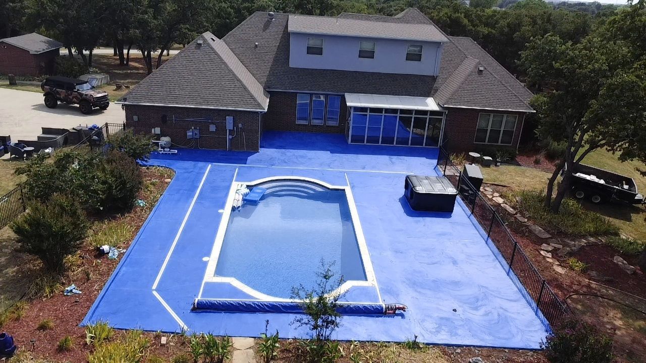 Aerial view of a blue backyard pool deck beside a house and trees