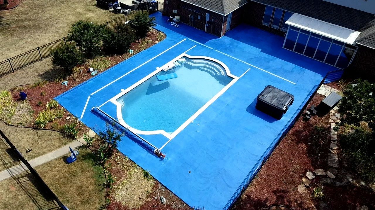Aerial view of a blue outdoor pool deck with a white-covered pool and nearby buildings