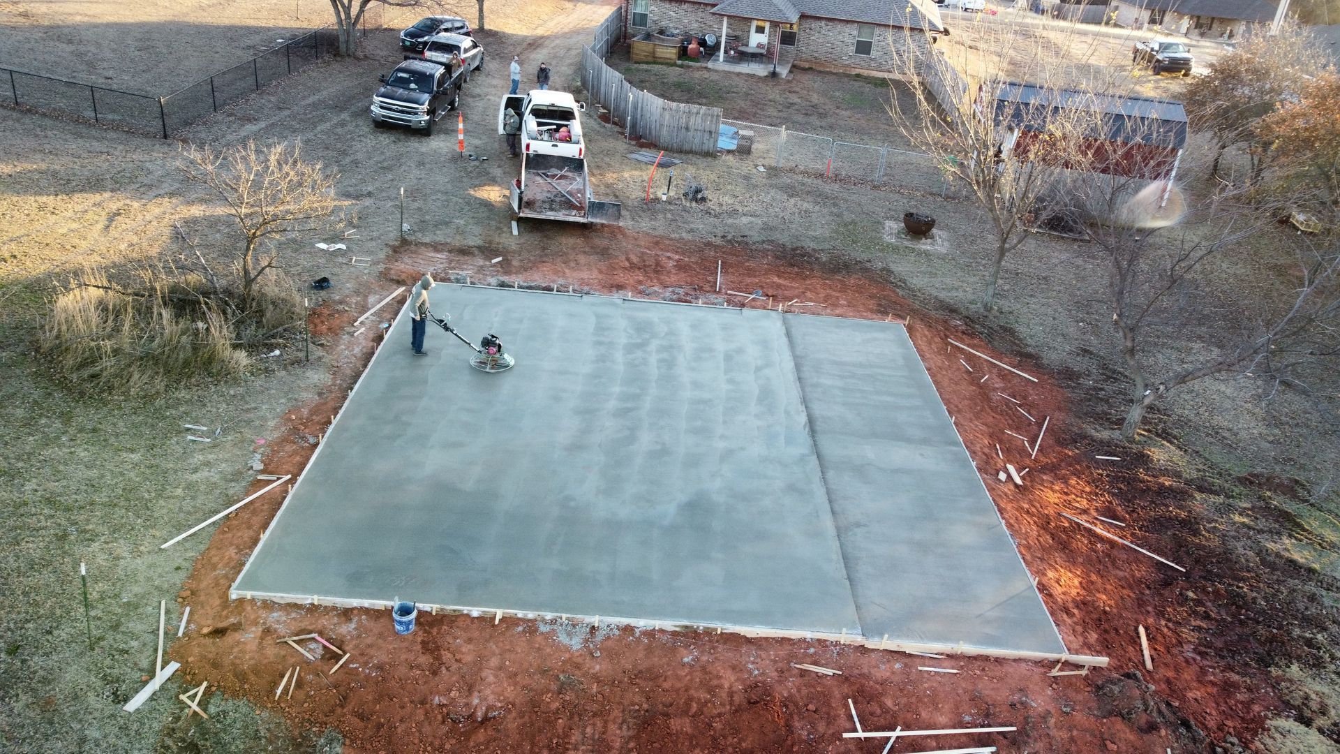 Concrete slab under construction with two workers, surrounded by dirt and equipment