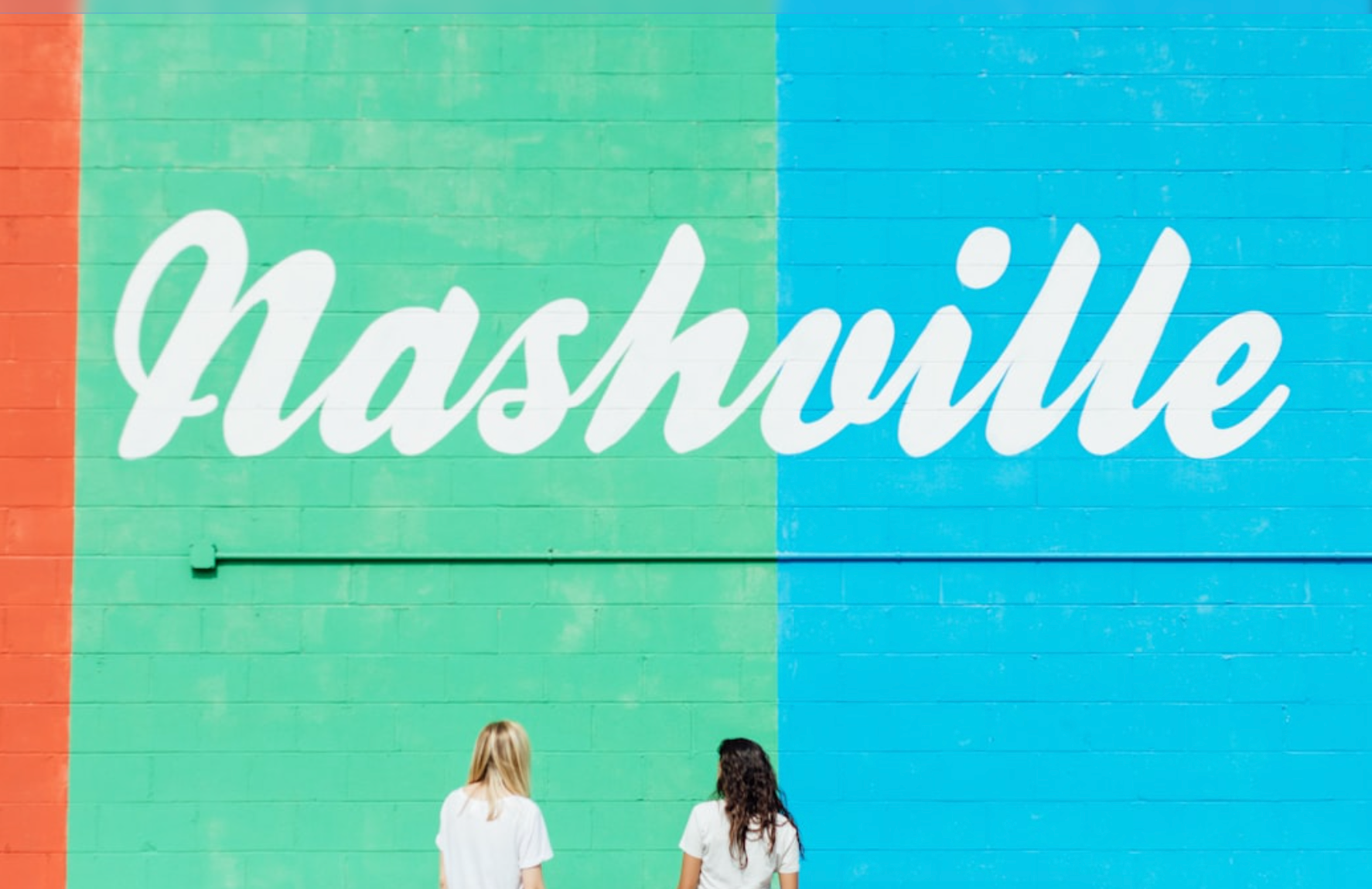 Two people in front of a Nashville mural on a colorful wall.