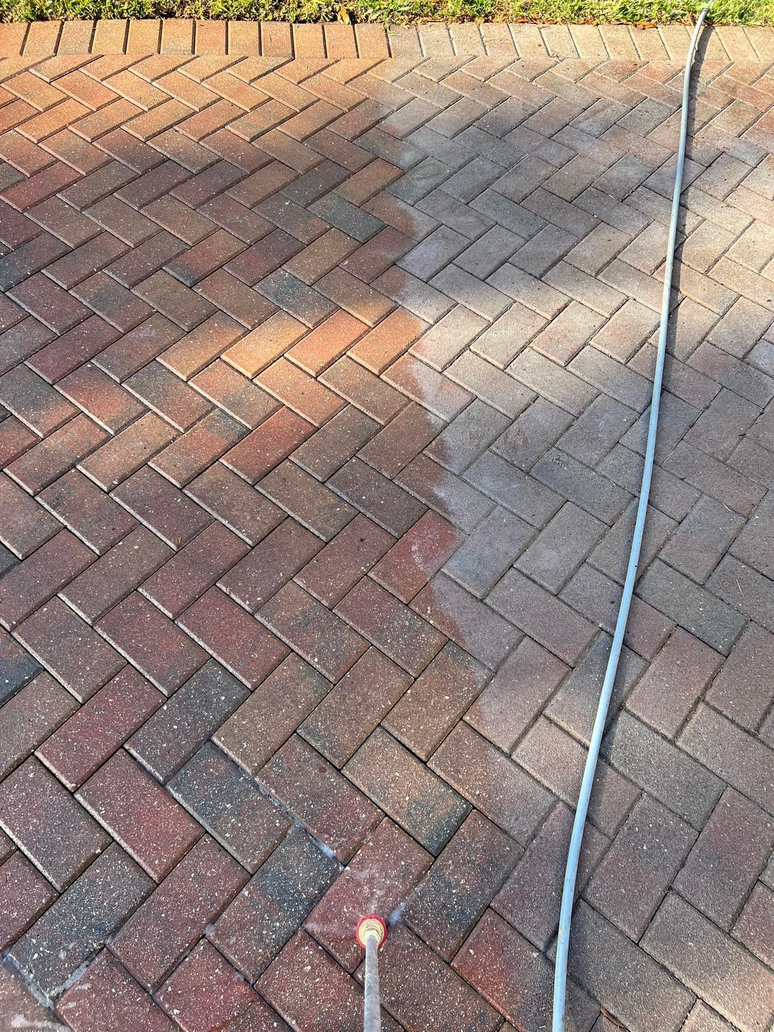A brick walkway being pressure washed; clean side is lighter, revealing color.
