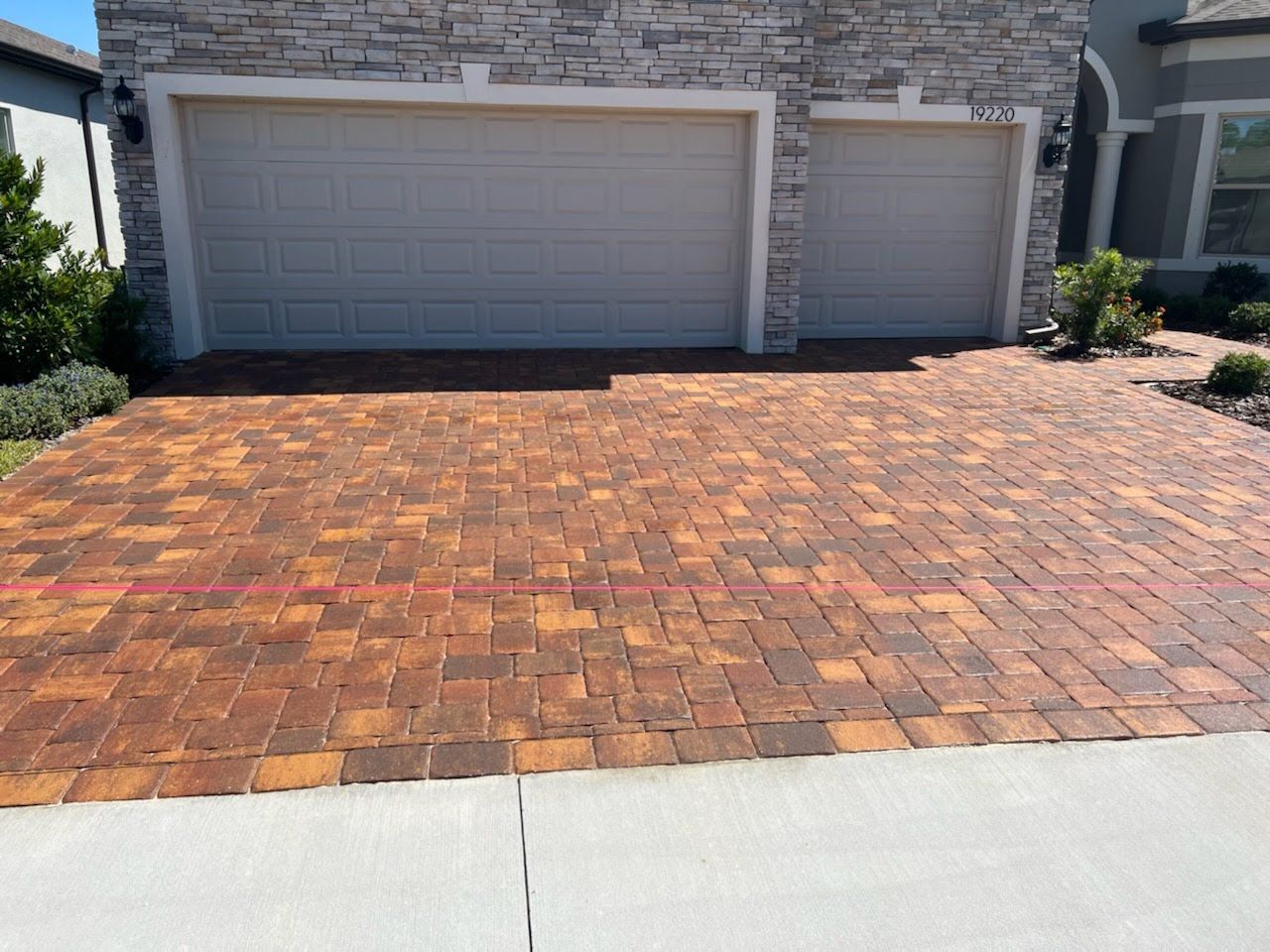 Brick driveway leading to a light tan garage with a stone facade.
