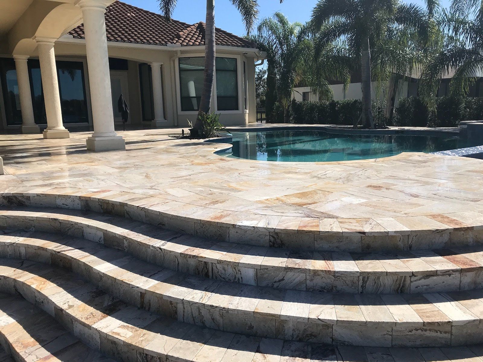 Stone steps leading up to a pool patio with a house in the background.