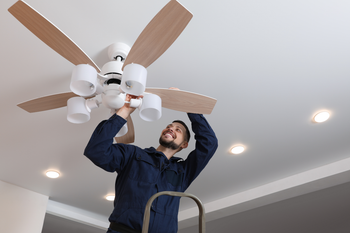 A man is standing on a ladder fixing a ceiling fan.