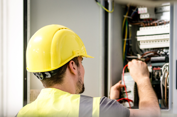 A man wearing a hard hat and safety vest is working on an electrical box.